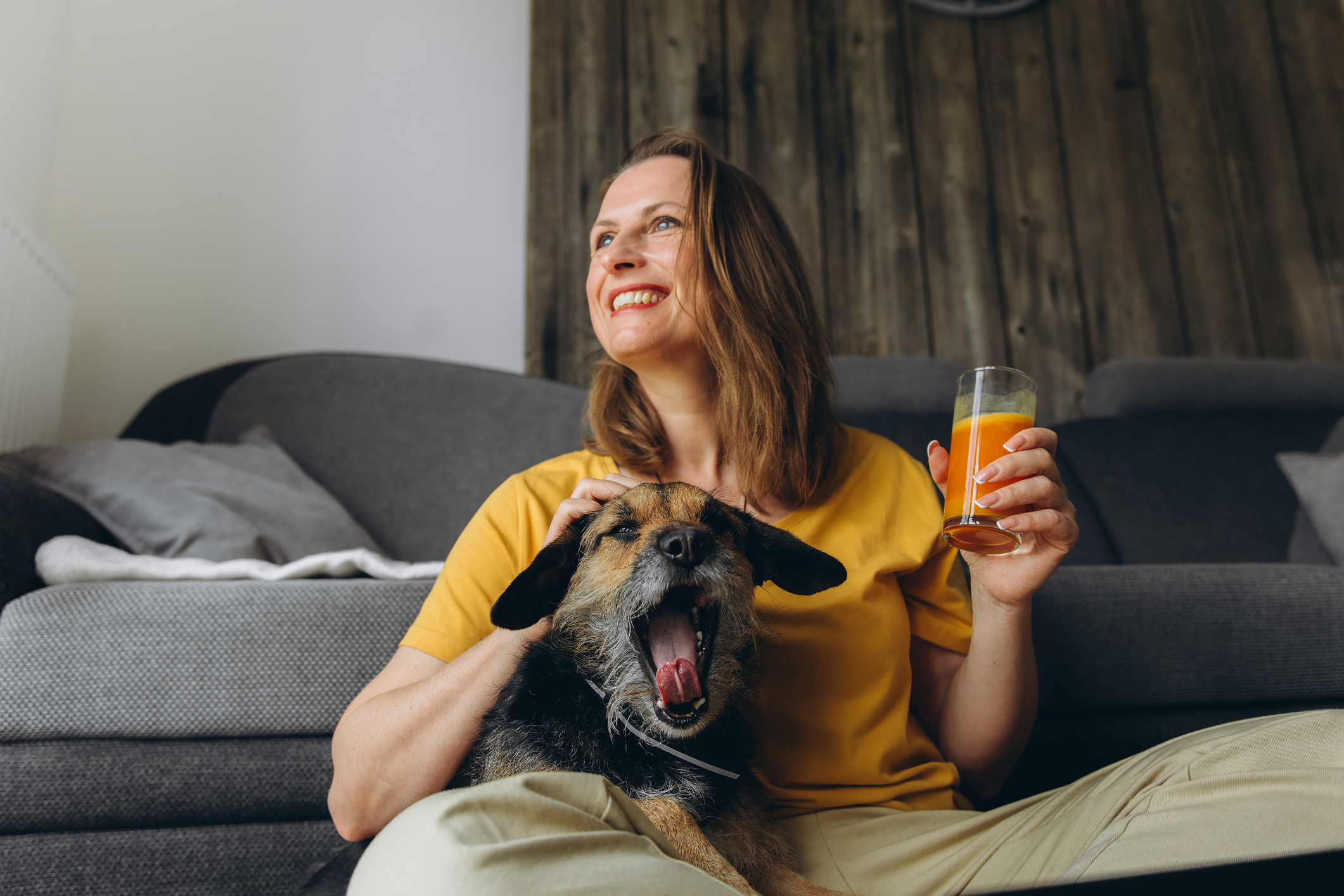 A smiling woman relaxing at home with her dog and a glass of fresh juice, supporting her immune health before cold season