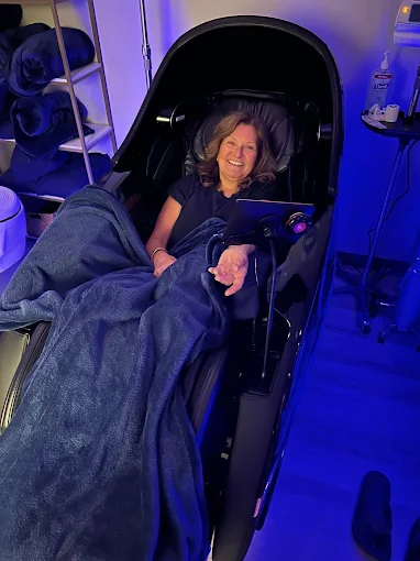 Guest relaxing in a zero-gravity recovery chair under blue ambient light